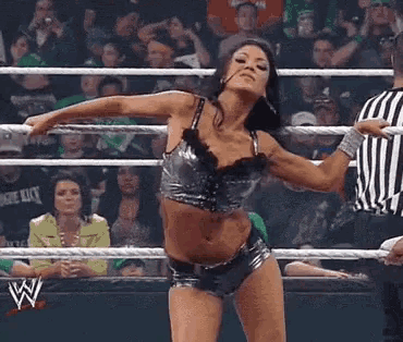 a woman is dancing in a wrestling ring while a referee looks on .