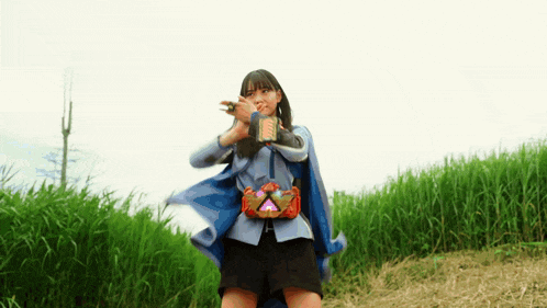 a woman in a cape is standing in a field of tall grass holding a sword .