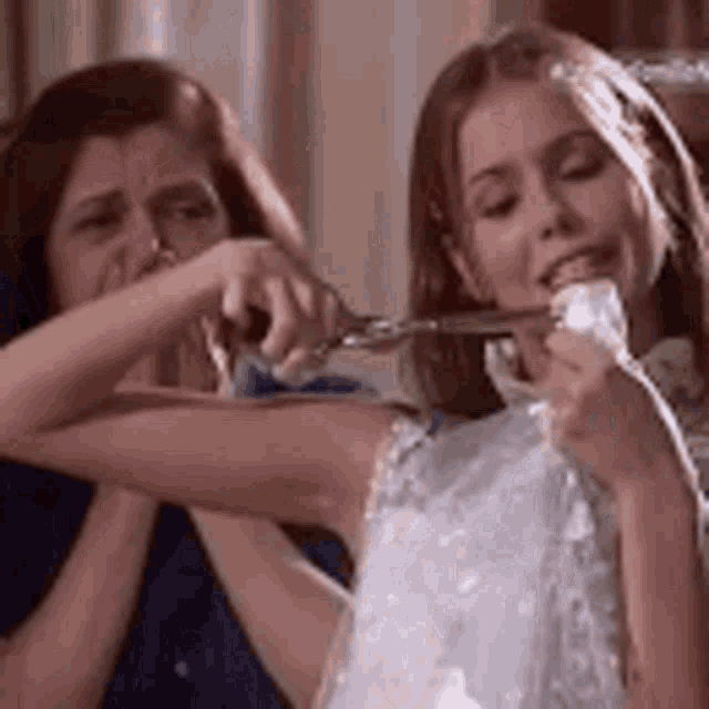 a woman is cutting a piece of cake with a pair of scissors while another woman watches .