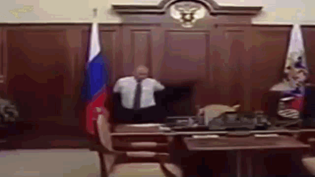 a man in a suit and tie is standing in front of a desk with a russian flag behind him .