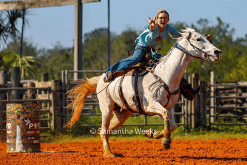 a woman is riding a white horse in a rodeo arena with a barrel that says pk on it