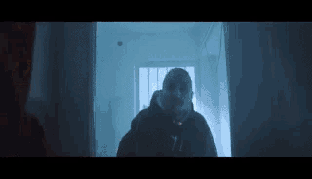 a man in a hooded jacket is standing in a dark hallway in front of a window .