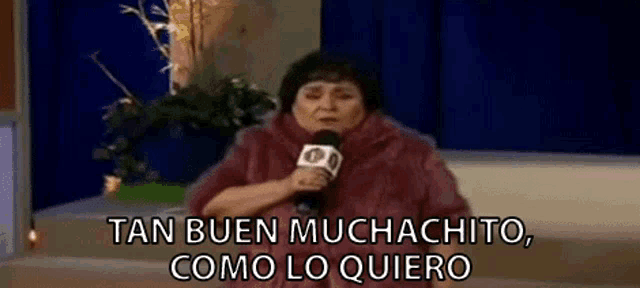 a woman is holding a microphone and saying `` tan buen muchacho , como lo quiero '' .