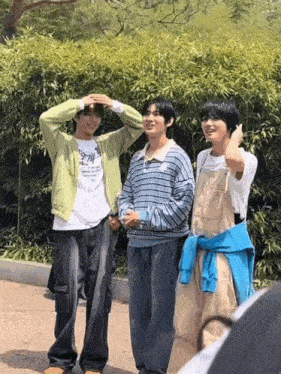 three young men are standing next to each other in front of a bamboo wall .