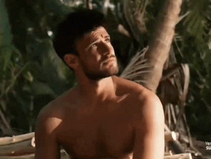 a shirtless man with a beard is sitting in front of a tree .