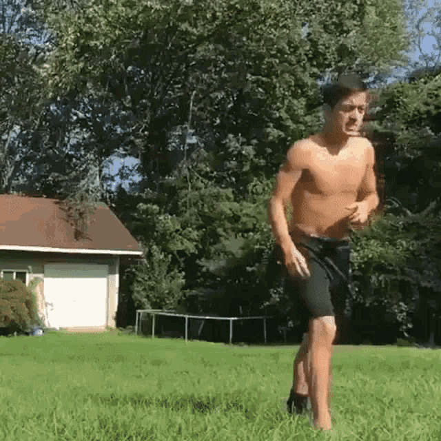 a shirtless man is running in the grass in front of a house .