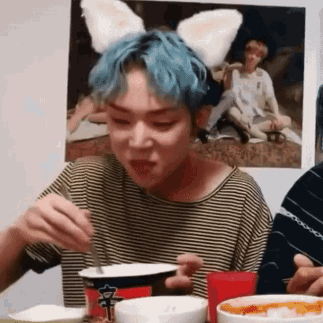 a man with blue hair and bunny ears is eating a bowl of food with a fork .