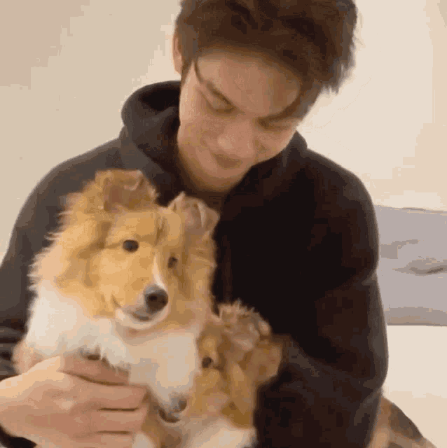 a man in a black hoodie is holding a small dog in his arms .