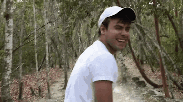 a man wearing a white hat and a white shirt is walking through a forest .