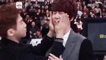 a man in a suit is touching another man 's face in front of a crowd .