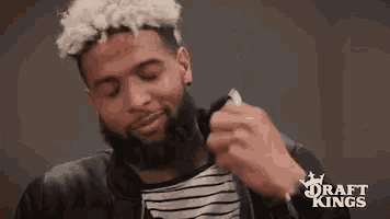 a man with a beard is wearing a black jacket and a striped shirt while holding a necklace .