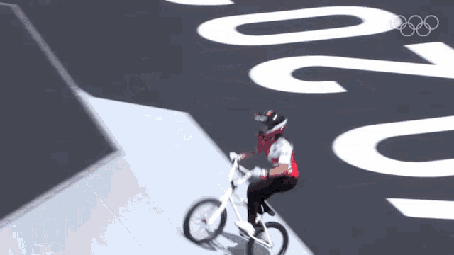 a person is riding a bike on a road with the olympic rings in the background