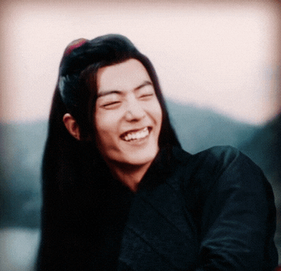 a young man with long hair is laughing with his eyes closed .