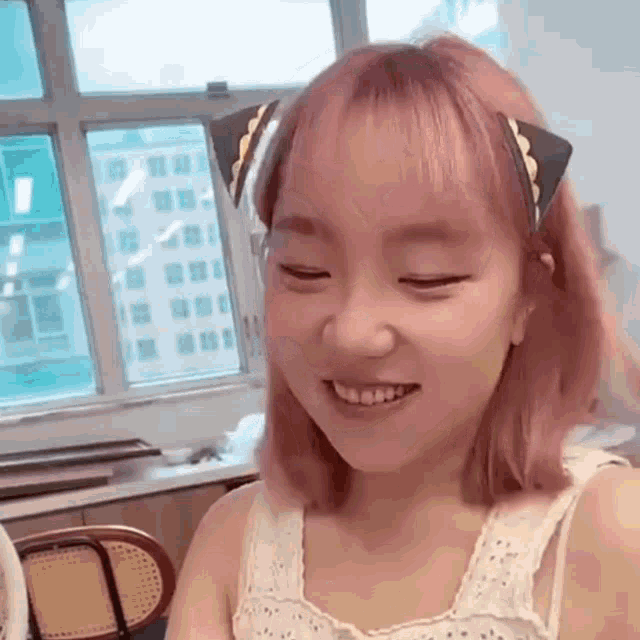a girl with pink hair is wearing a headband with cat ears on it .