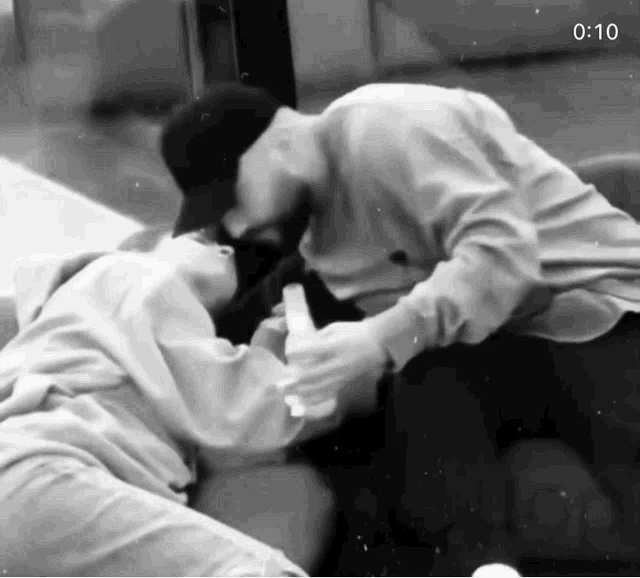 a black and white photo of a man and a woman kissing .