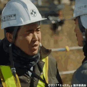 a man wearing a hard hat and safety vest is talking to another man .