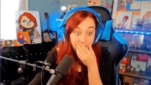 a woman with red hair is wearing headphones and sitting in front of a microphone covering her mouth .