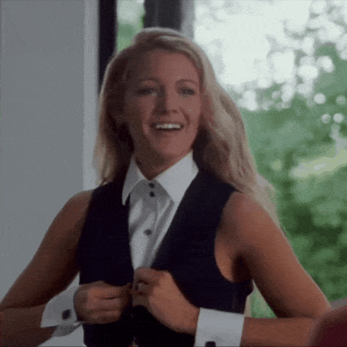a woman wearing a tuxedo vest and a white shirt smiles
