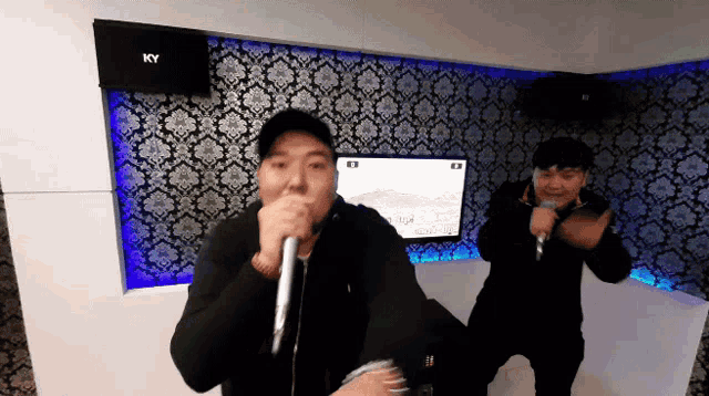 two men singing into microphones in front of a ky box