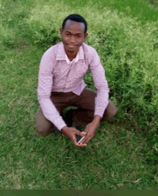 a man in a pink shirt is kneeling in the grass