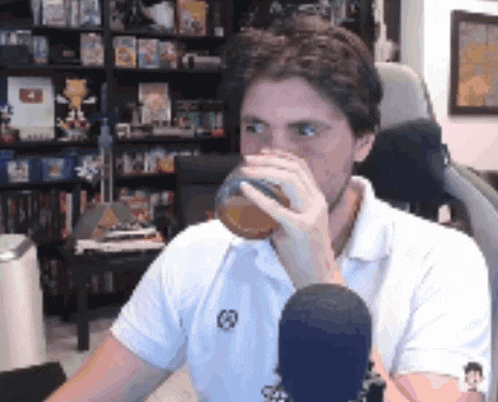 a man in a white shirt is drinking from a glass while sitting in front of a microphone