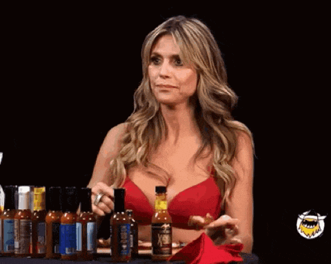 a woman in a red bra is sitting at a table with a bunch of hot sauce bottles .