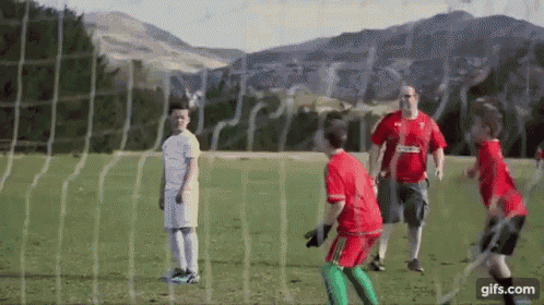 a group of kids are playing soccer on a field with mountains in the background .