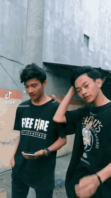 two young men are standing next to each other in front of a building wearing free fire shirts .