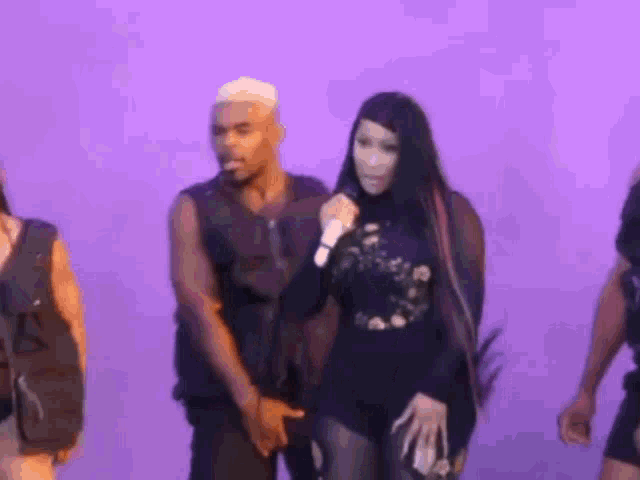 a woman is singing into a microphone while standing next to a man on a stage in front of a purple background .