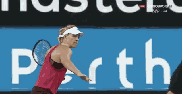 a woman is holding a tennis racquet in front of a sign that says perth
