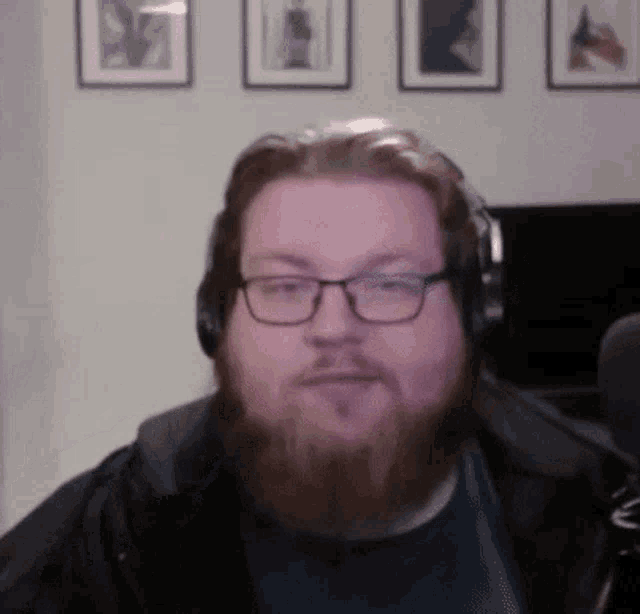 a man with a beard and glasses is wearing headphones and a jacket .