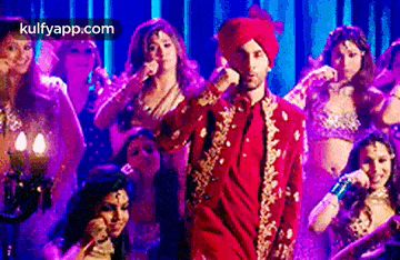 a man in a red suit and turban is singing into a microphone .