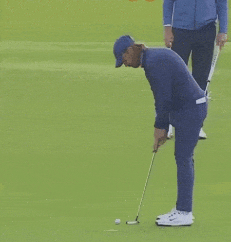 a man in a blue shirt is putting a golf ball