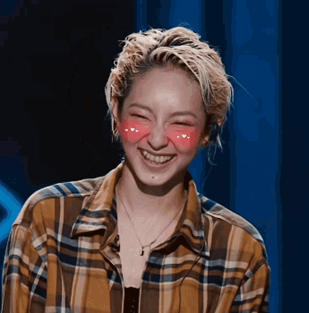 a woman wearing a plaid shirt and a necklace is smiling with hearts on her cheeks