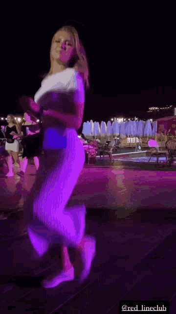 a woman in a white dress is dancing in a dark room with purple lights behind her