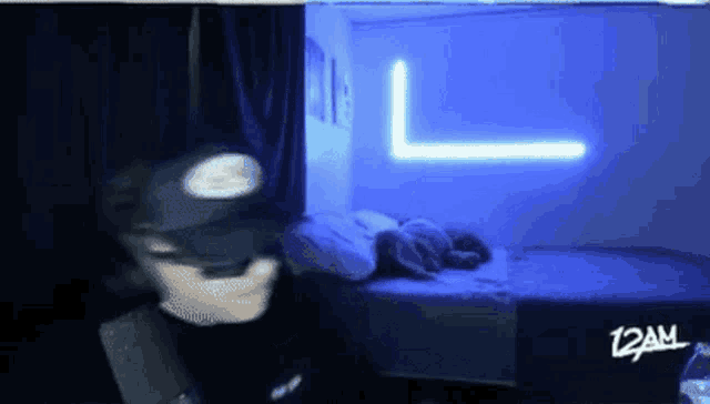 a person wearing a batman mask is standing in front of a bed with the time 12am