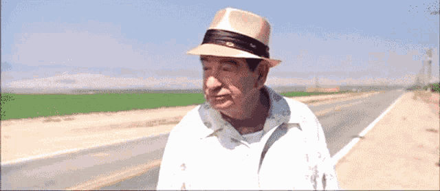 a man wearing a hat and a white shirt is walking down a road