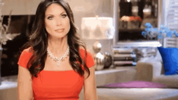 a woman in a red dress and a pearl necklace is sitting on a couch in a living room .