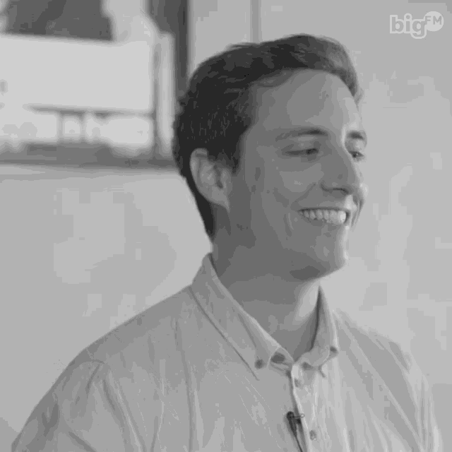 a man in a white shirt is smiling in a black and white photo with the big tv logo behind him