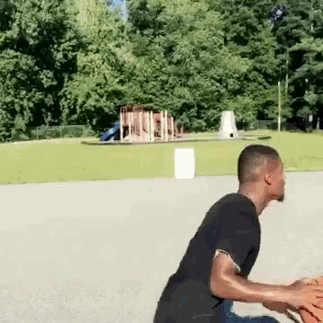 a man in a black shirt is playing basketball in a park with a playground in the background