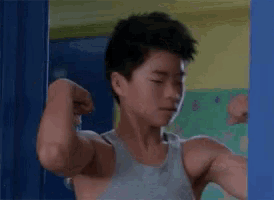 a man in a tank top is flexing his muscles in front of a mirror