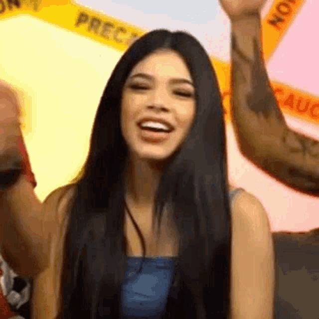a woman with long black hair is smiling while standing in front of a yellow caution tape .