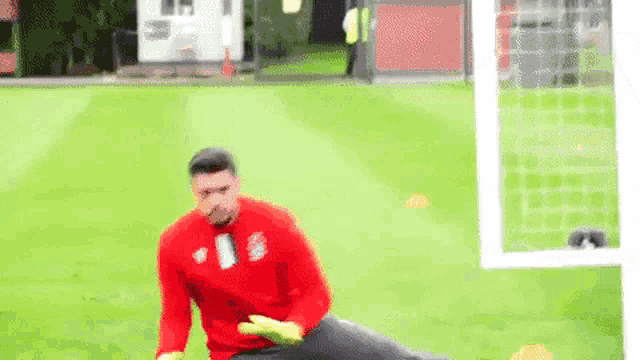 a soccer goalie is stretching on the field while wearing gloves .