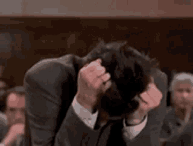 a man in a suit is scratching his head in a crowded room .