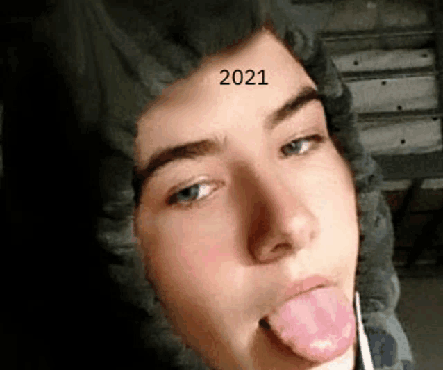 a young man wearing a hooded jacket is sticking his tongue out and making a funny face .