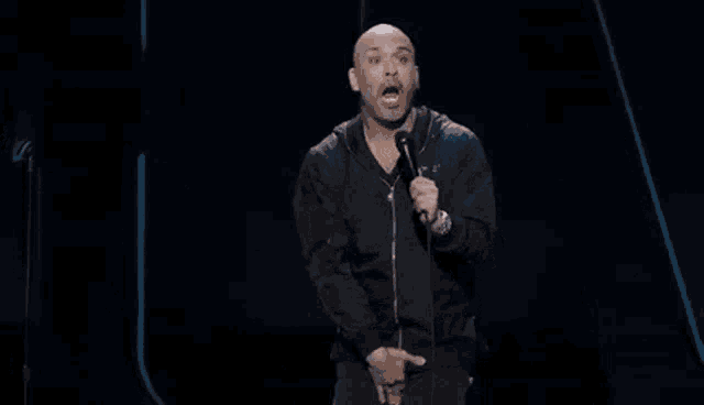 a bald man is kneeling down in front of a microphone and giving a speech .
