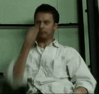a man in a white shirt is sitting in a chair and rubbing his nose .