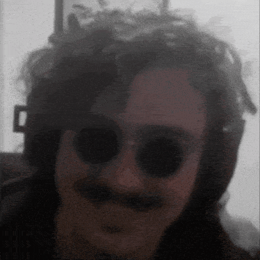 a man with a mustache and sunglasses is looking at the camera