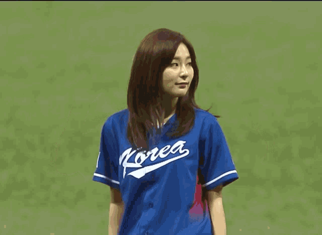 a woman wearing a blue korea jersey is throwing a baseball