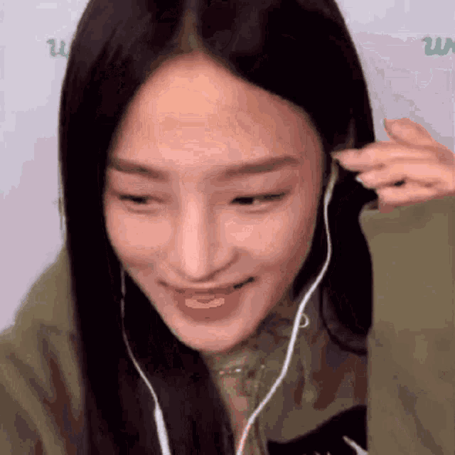 a woman wearing headphones and a green jacket is smiling and looking at the camera .